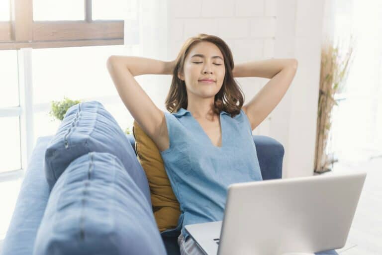 Asian businesswoman using laptop work at home stretch relax breathe fresh air on sofa.