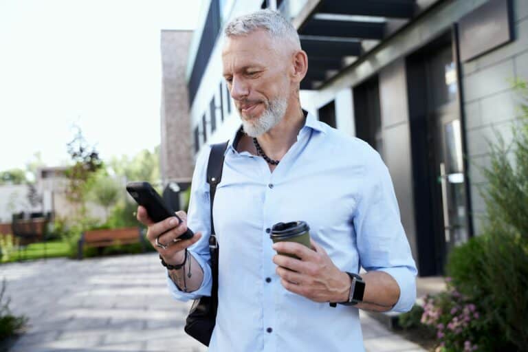 Stay connected. Modern middle aged businessman using his smartphone while walking outdoors with a